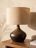 Lampe de table Golva en céramique bronze et abat-jour en lin beige, posée sur une console